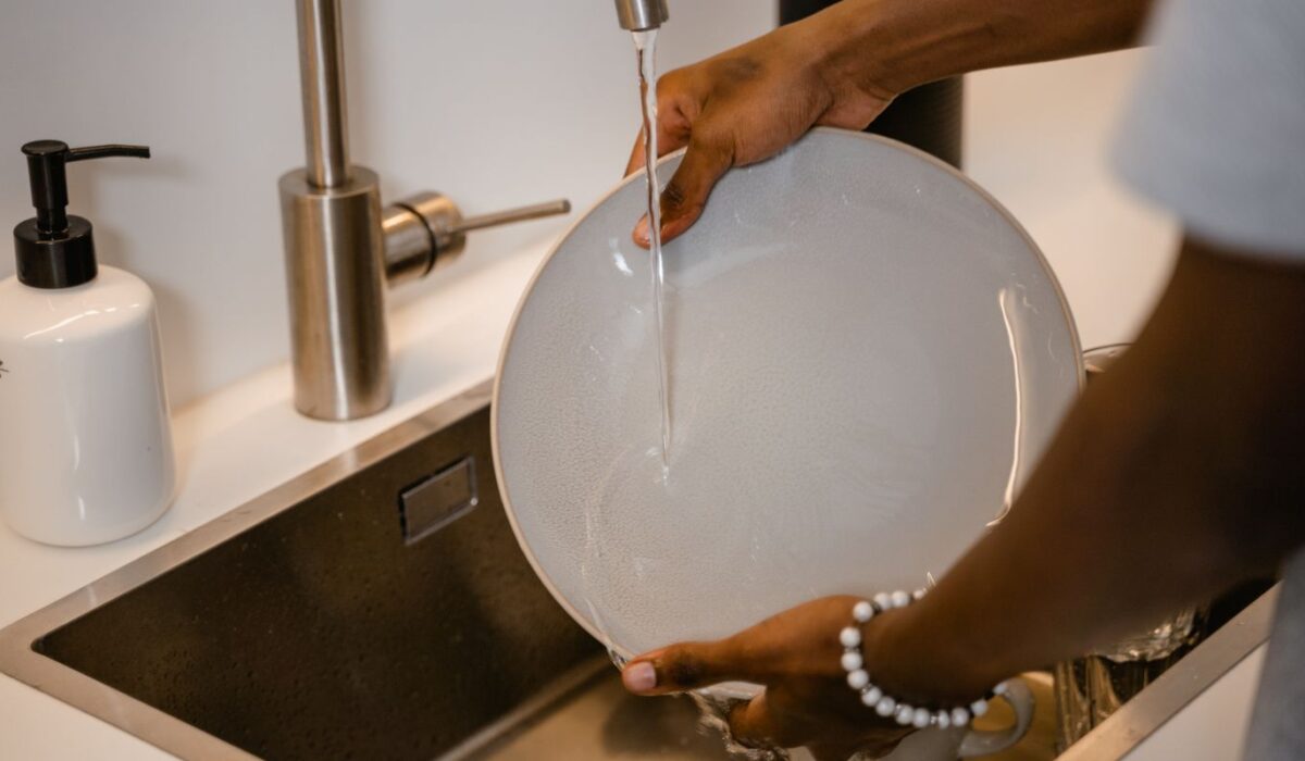 Person hand washing a plate under running water at a kitchen sink