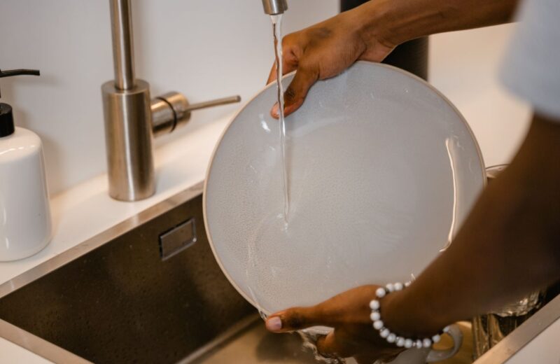 Person hand washing a plate under running water at a kitchen sink