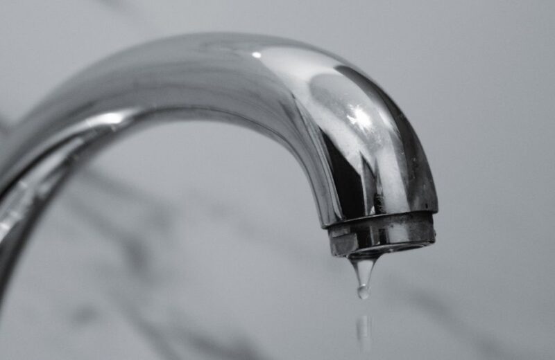Chrome bathroom faucet with a single water droplet forming at the spout, illustrating a slow leak