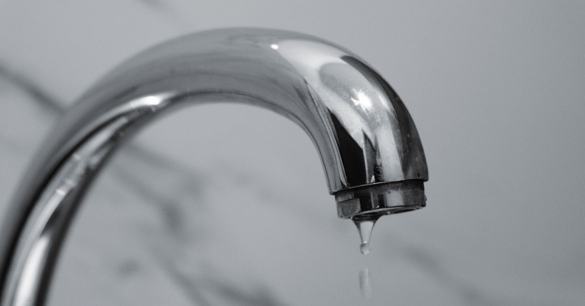 Chrome bathroom faucet with a single water droplet forming at the spout, illustrating a slow leak