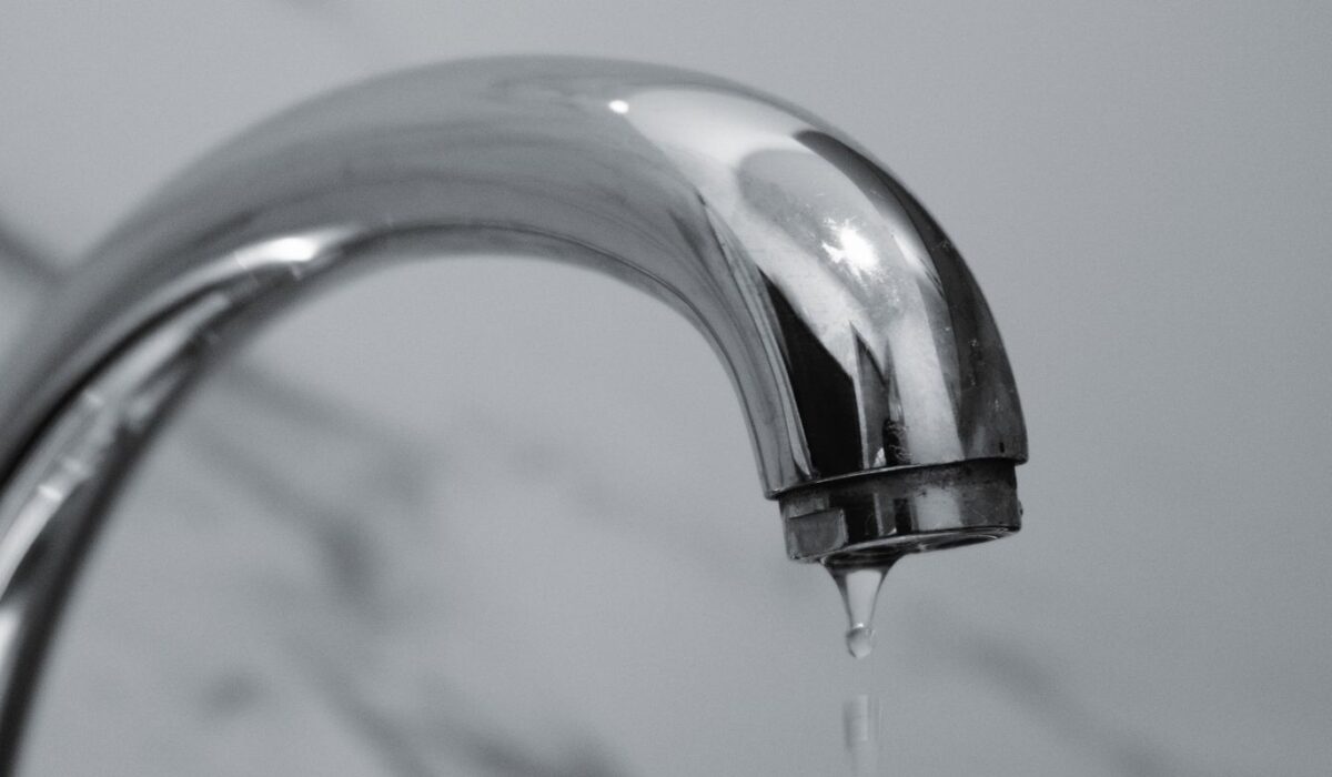 Chrome bathroom faucet with a water droplet hanging from the spout, illustrating the small drips that create phantom water use in a home.