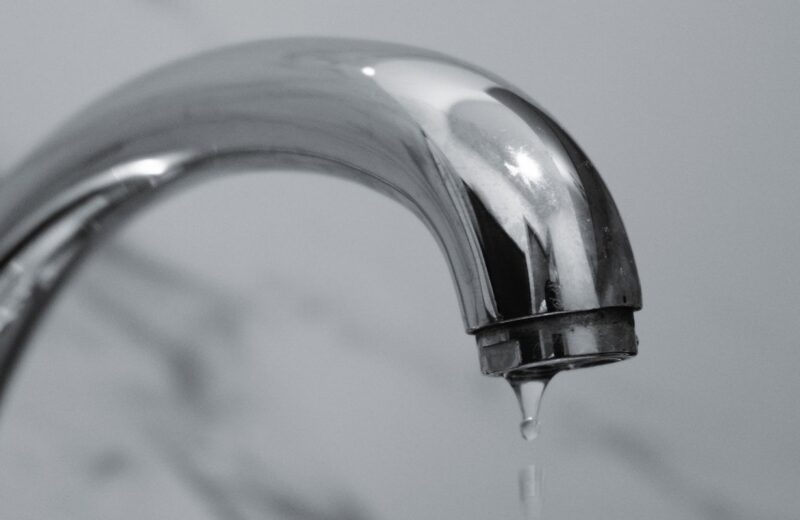 Chrome bathroom faucet with a water droplet hanging from the spout, illustrating the small drips that create phantom water use in a home.