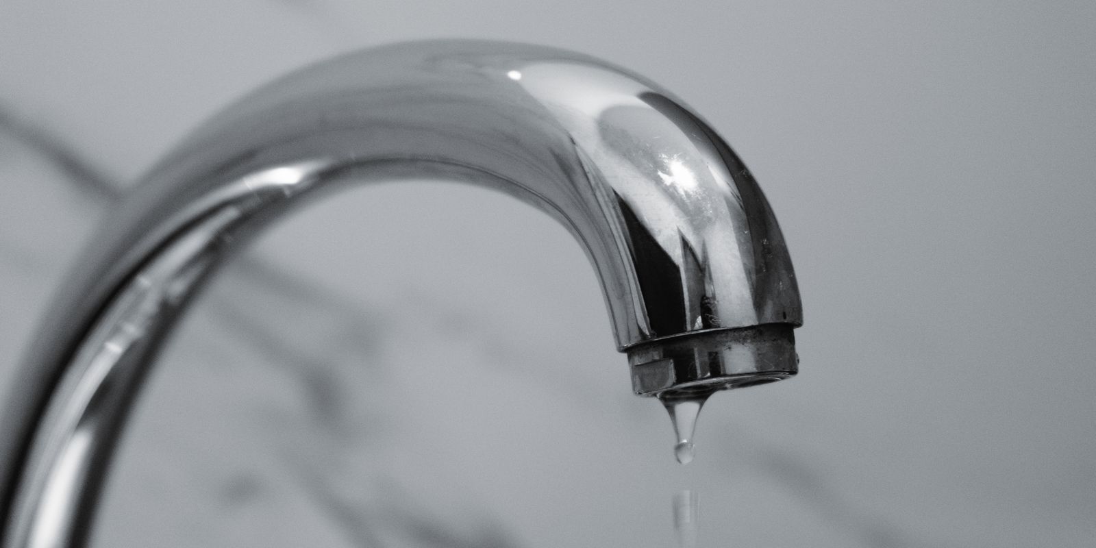 Chrome bathroom faucet with a water droplet hanging from the spout, illustrating the small drips that create phantom water use in a home.