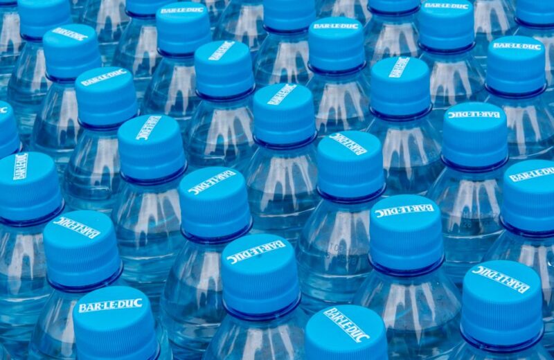Stack of clear plastic water bottles with blue caps illustrating single-use bottled water waste