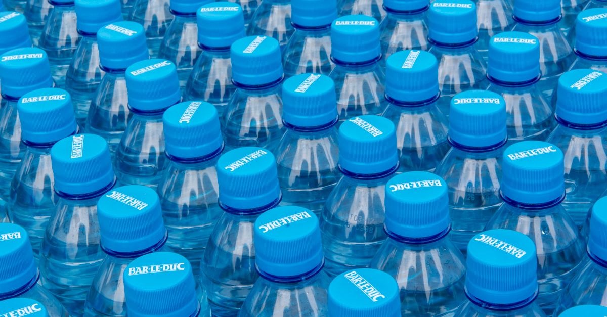 Stack of clear plastic water bottles with blue caps illustrating single-use bottled water waste