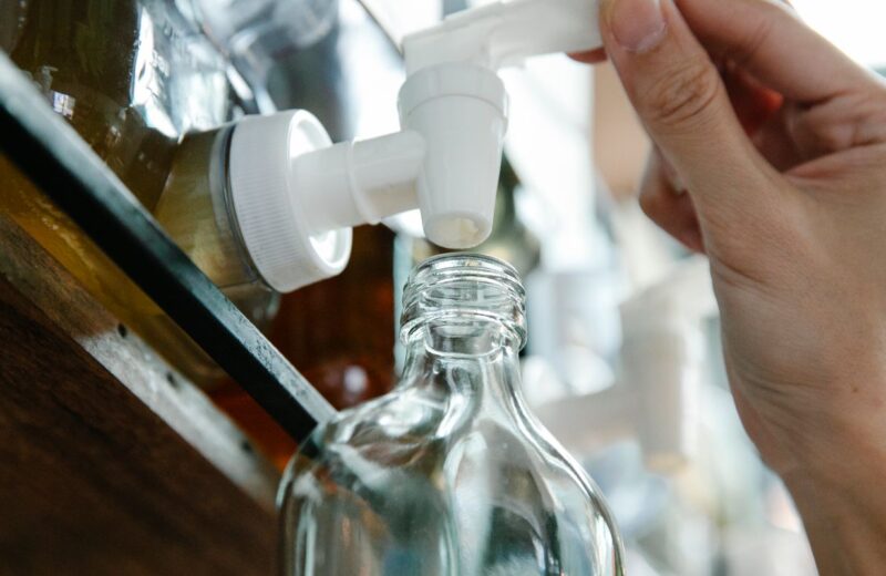 Hand refilling a glass cleaning-solution bottle from a pump dispenser on a kitchen counter.