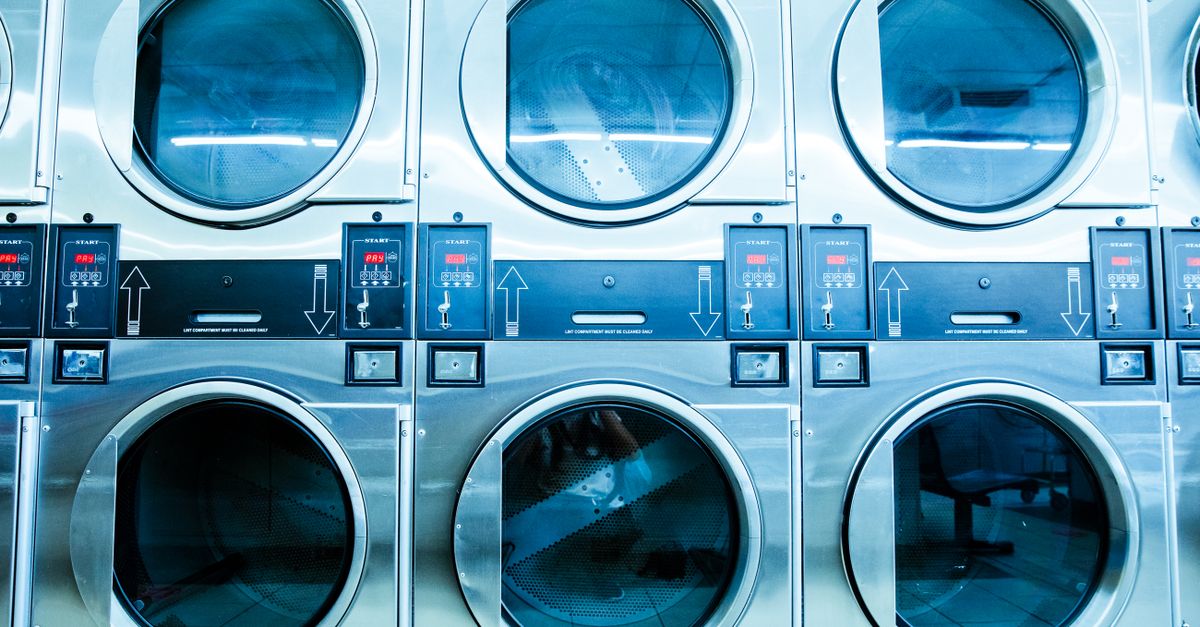 Row of modern front-loading washing machines in a bright launderette, showing cycle selector dials and door windows.